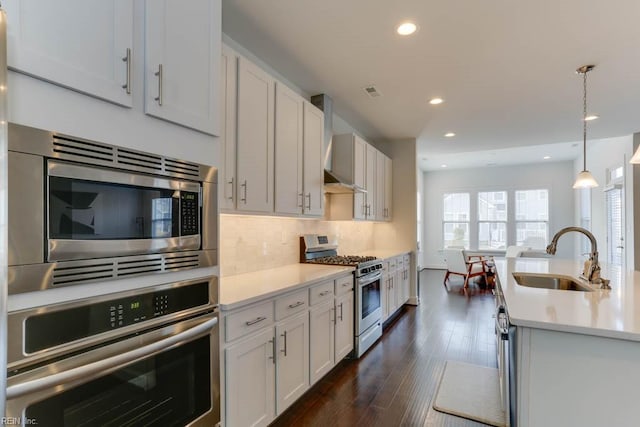 kitchen with a sink, stainless steel appliances, light countertops, wall chimney range hood, and backsplash