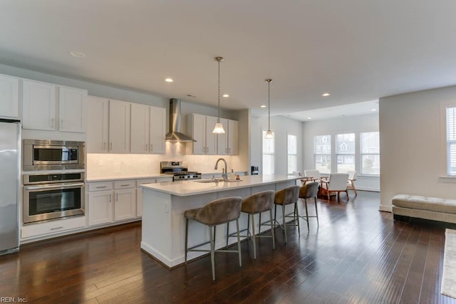 kitchen with tasteful backsplash, wall chimney exhaust hood, appliances with stainless steel finishes, a breakfast bar, and a sink