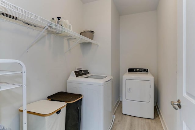 clothes washing area featuring laundry area, separate washer and dryer, light wood-type flooring, and baseboards