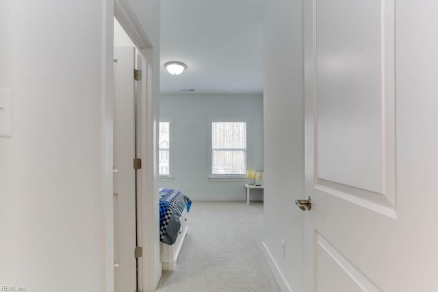 corridor featuring light colored carpet and baseboards