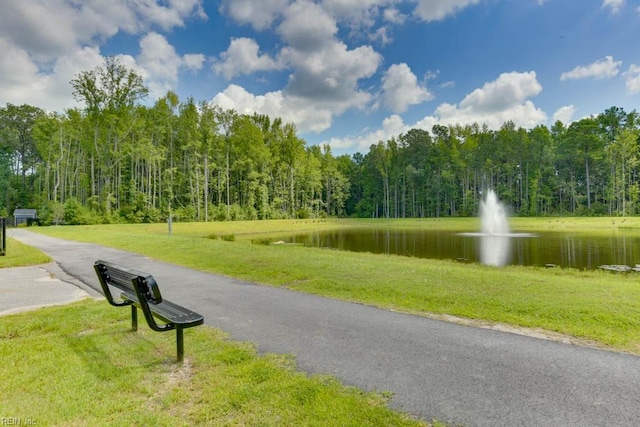 view of property's community with aphalt driveway, a water view, a lawn, and a view of trees