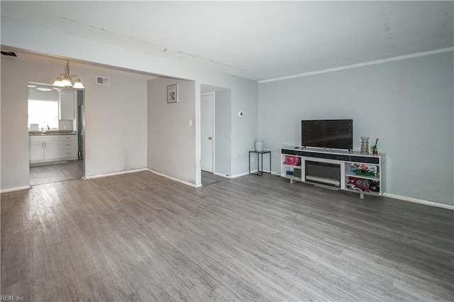 unfurnished living room featuring an inviting chandelier, baseboards, visible vents, and wood finished floors