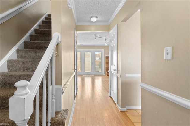 hall featuring french doors, light wood-style flooring, ornamental molding, a textured ceiling, and stairs