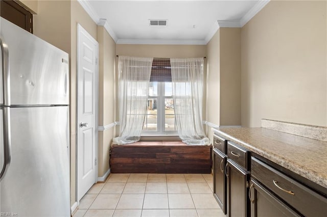 kitchen featuring crown molding, visible vents, freestanding refrigerator, light tile patterned flooring, and dark brown cabinetry