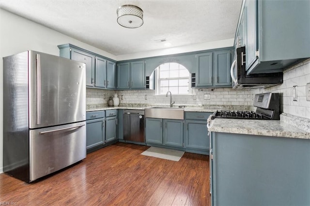 kitchen with tasteful backsplash, appliances with stainless steel finishes, dark wood-style flooring, and a sink