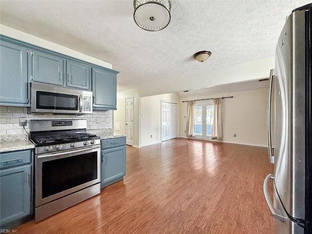 kitchen with appliances with stainless steel finishes, blue cabinets, decorative backsplash, and light wood finished floors