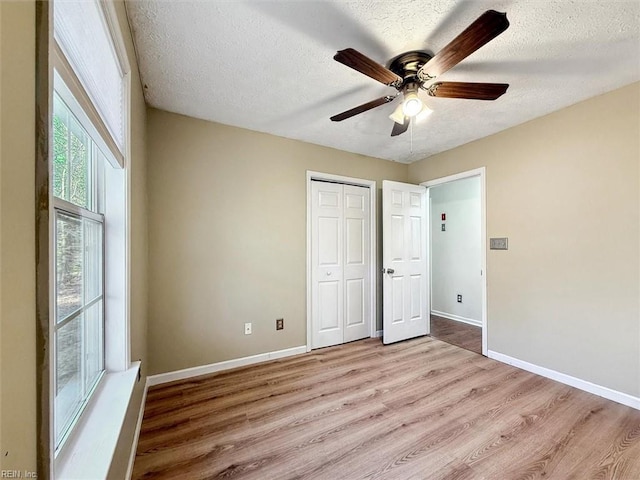 unfurnished bedroom with light wood-style floors, a closet, a textured ceiling, and baseboards