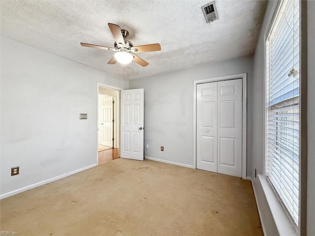 unfurnished bedroom featuring a textured ceiling, light carpet, visible vents, baseboards, and a closet