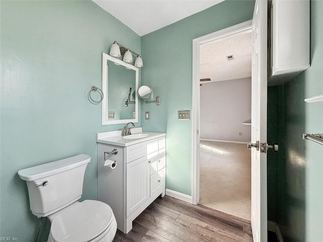 half bath featuring toilet, baseboards, wood finished floors, and vanity