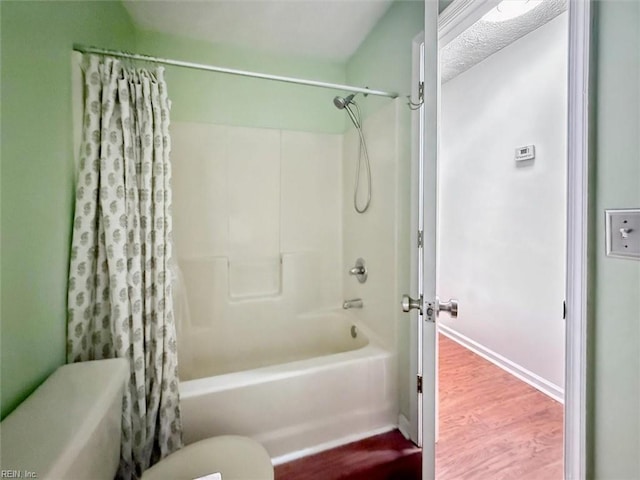 bathroom featuring baseboards, shower / bathtub combination with curtain, toilet, and wood finished floors