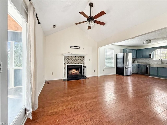 unfurnished living room with ceiling fan, a fireplace, a sink, baseboards, and dark wood-style floors