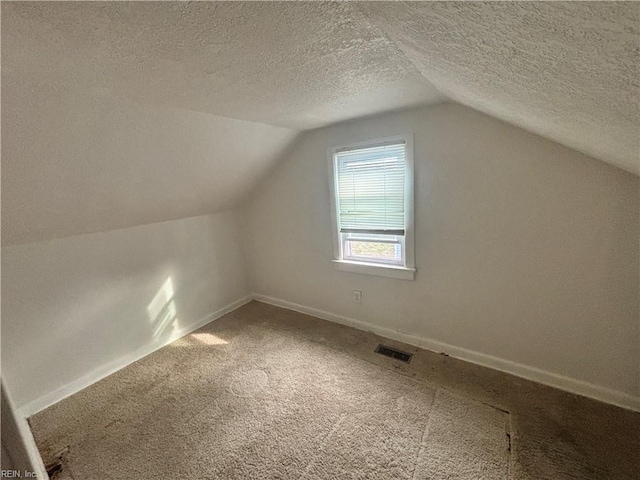 additional living space with baseboards, visible vents, vaulted ceiling, a textured ceiling, and carpet floors