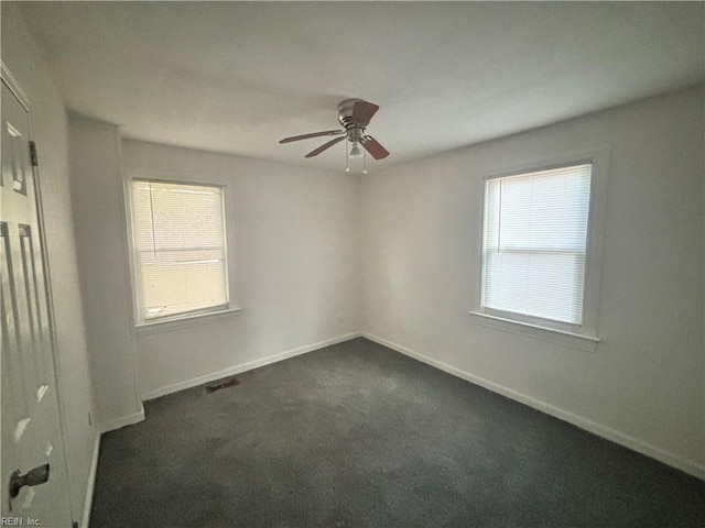 spare room featuring ceiling fan, visible vents, baseboards, and dark colored carpet