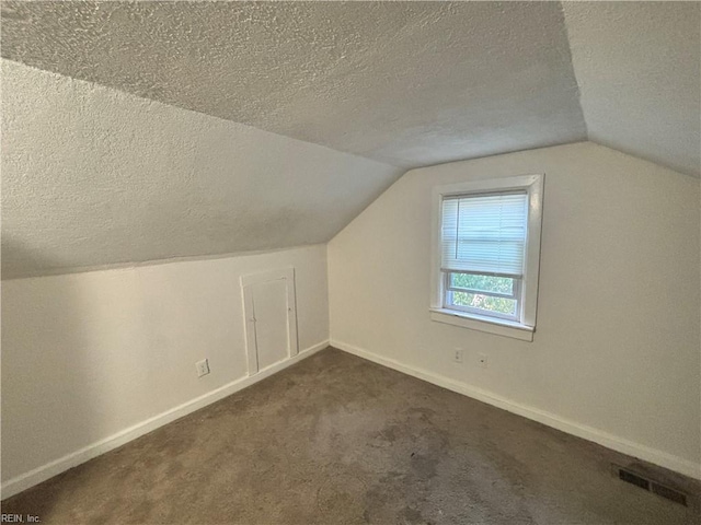 additional living space featuring visible vents, dark carpet, vaulted ceiling, a textured ceiling, and baseboards