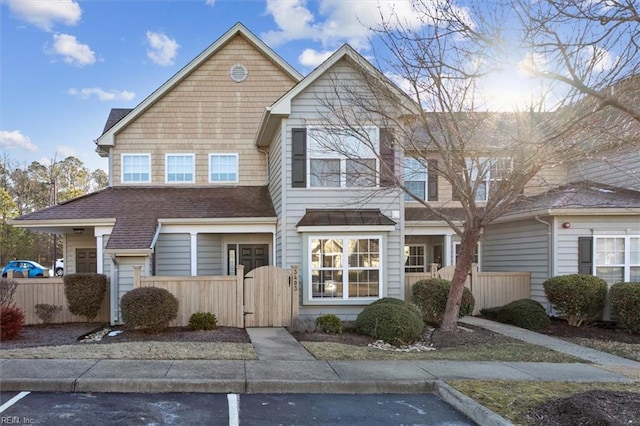 multi unit property featuring a fenced front yard, a gate, uncovered parking, and a shingled roof