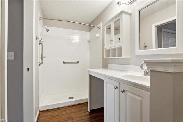 full bathroom featuring a tile shower, a textured ceiling, vanity, and wood finished floors