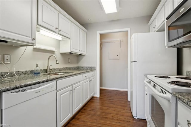 kitchen with white appliances, white cabinets, dark wood-style floors, light stone counters, and a sink