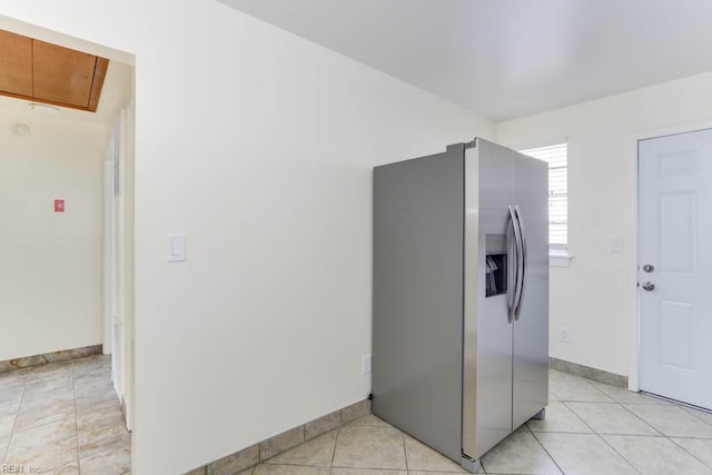 kitchen featuring brown cabinets, stainless steel fridge, baseboards, and light tile patterned flooring