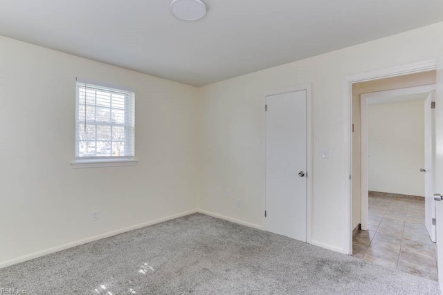 tiled spare room featuring carpet floors and baseboards