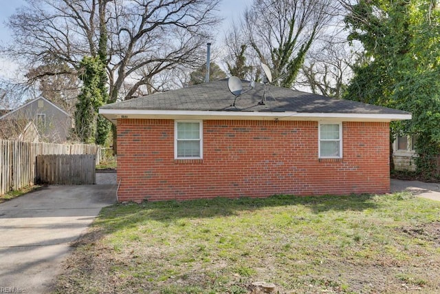 view of side of home featuring fence, a lawn, and brick siding