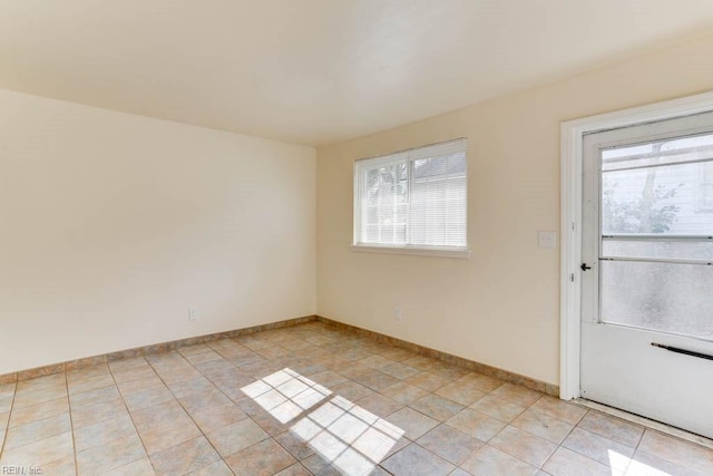 empty room featuring a wealth of natural light, light tile patterned flooring, and baseboards