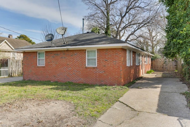 view of side of home with a yard, fence, and brick siding