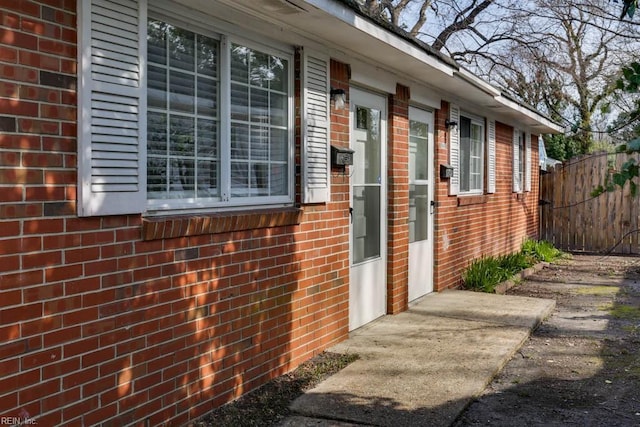 view of exterior entry with brick siding and fence