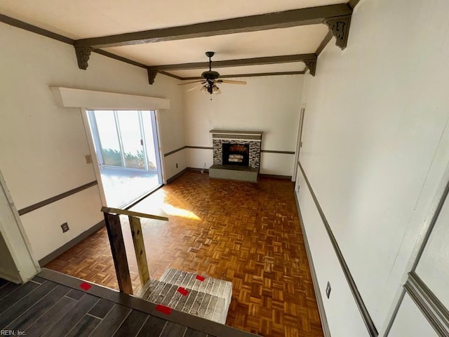 unfurnished living room with a fireplace with raised hearth, ceiling fan, beamed ceiling, and baseboards