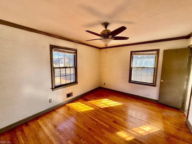 spare room featuring plenty of natural light, crown molding, baseboards, and wood finished floors