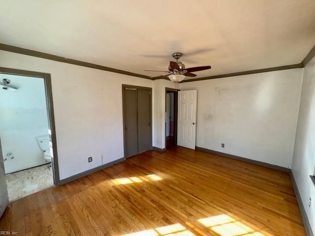 unfurnished bedroom with baseboards, ensuite bath, wood finished floors, and crown molding