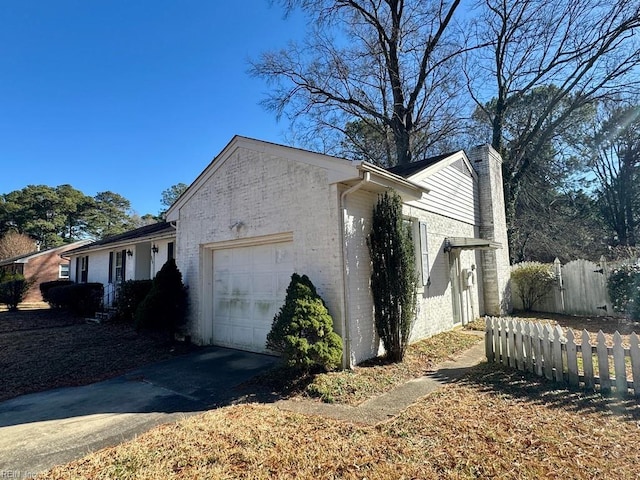 view of side of property with aphalt driveway, brick siding, a chimney, fence, and a garage