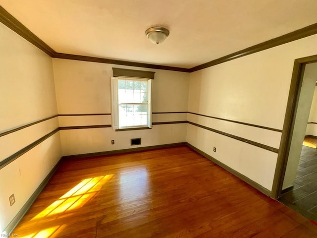 spare room featuring crown molding, wood finished floors, visible vents, and baseboards