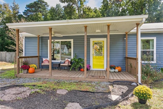 property entrance featuring covered porch, ceiling fan, and fence