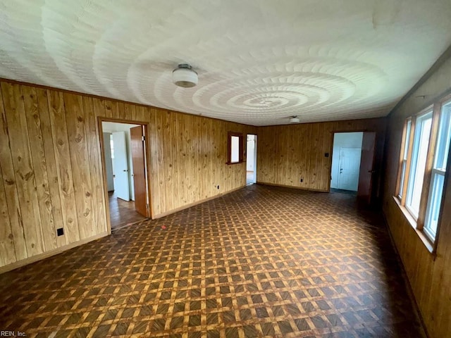 empty room featuring wooden walls, baseboards, and dark floors