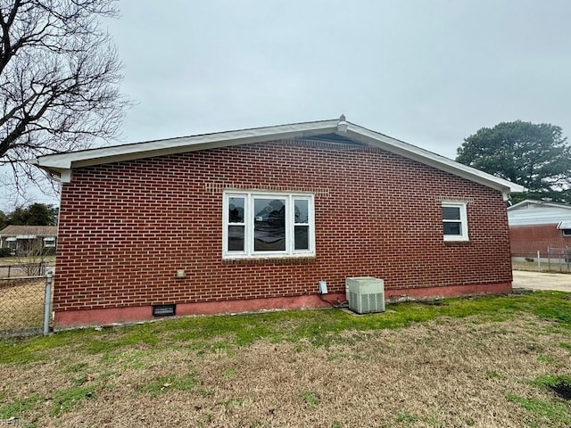 view of home's exterior with a yard, fence, central AC, and brick siding