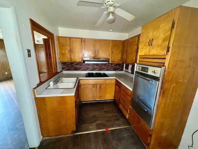 kitchen featuring light countertops, brown cabinetry, a sink, black gas stovetop, and under cabinet range hood