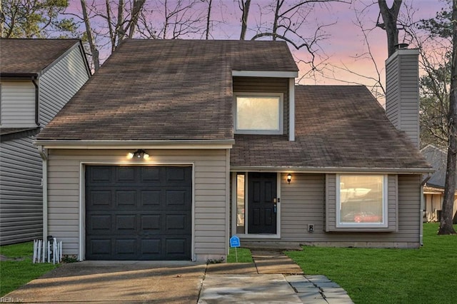 view of front of property featuring a garage, driveway, a lawn, roof with shingles, and a chimney