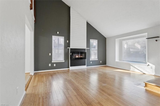 unfurnished living room featuring baseboards, a fireplace, high vaulted ceiling, and hardwood / wood-style floors