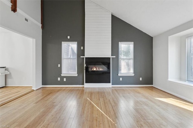 unfurnished living room with a large fireplace, wood-type flooring, high vaulted ceiling, and baseboards