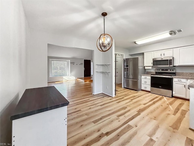 kitchen with appliances with stainless steel finishes, an inviting chandelier, light wood-style floors, white cabinetry, and pendant lighting