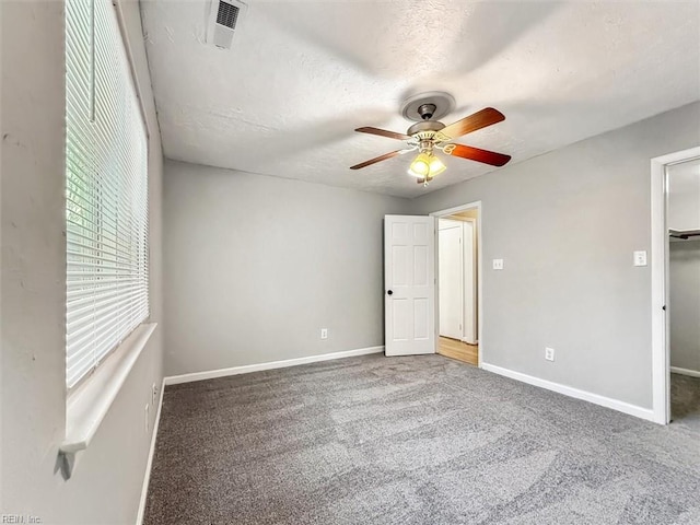 unfurnished bedroom featuring visible vents, baseboards, carpet, a walk in closet, and a textured ceiling