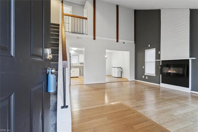 unfurnished living room with a large fireplace, visible vents, wood finished floors, stairs, and a high ceiling