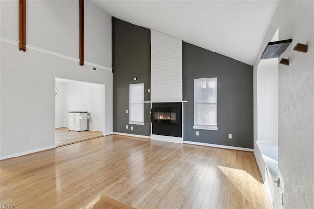 unfurnished living room featuring high vaulted ceiling, a fireplace, baseboards, and wood finished floors