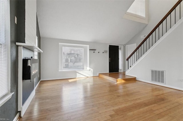 unfurnished living room featuring high vaulted ceiling, a fireplace, visible vents, stairs, and light wood finished floors