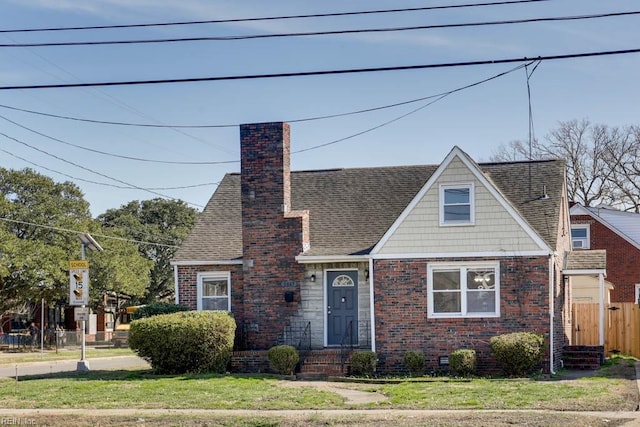 view of front of home featuring brick siding, a shingled roof, fence, a front lawn, and a chimney