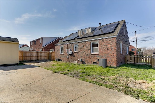 rear view of property with a yard, a fenced backyard, brick siding, and central AC