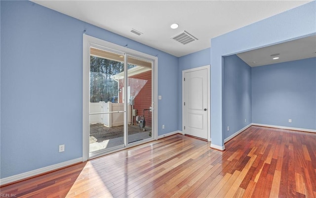 empty room featuring wood-type flooring, visible vents, and baseboards