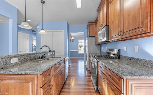 kitchen featuring brown cabinets, appliances with stainless steel finishes, dark wood-type flooring, a sink, and light stone countertops