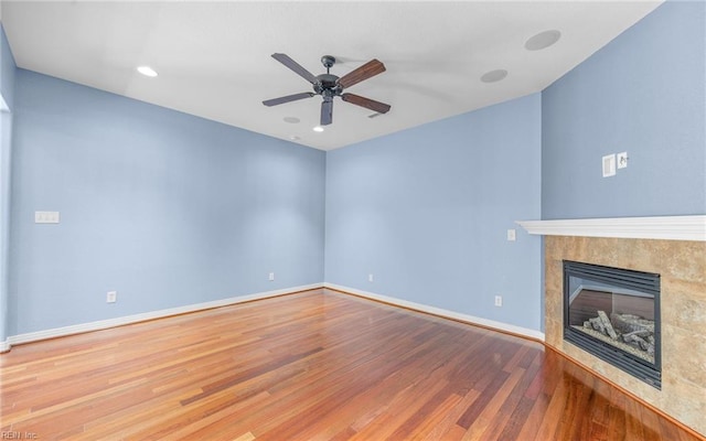 unfurnished living room featuring recessed lighting, wood finished floors, a ceiling fan, baseboards, and a tiled fireplace