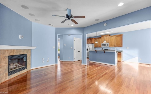 unfurnished living room featuring recessed lighting, light wood-style flooring, a ceiling fan, a tile fireplace, and baseboards